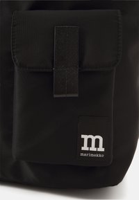 Zaino di tessuto nero con tasca anteriore a soffietto e design rettangolare. Presenta un'etichetta bianca con il logo "marimekko" e una texture di tessuto robusta.