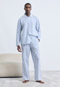 Set de pijamale din bumbac cu dungi în nuanțe de albastru, alb și verde. Include o cămașă cu butoni, cu mâneci lungi și pantaloni cu picioare largi. Textură netedă.