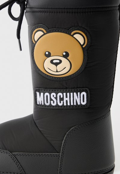 Svart vattentät stövel med en texturerad nedre sektion, prydd med en rund patch med en brun björnfans och "Moschino"-logotypen i vitt.