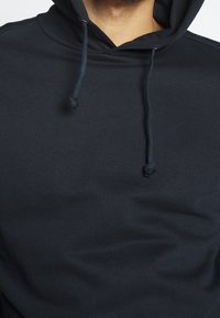 Felpa con cappuccio di un blu navy scuro realizzata in morbido tessuto misto cotone. Presenta un design classico con una tasca a marsupio frontale e un cappuccio con cordoncino regolabile.