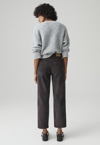 Light gray fluffy sweater with ribbed cuffs, paired with dark gray corduroy trousers featuring back pockets. Model wears dark shoes.