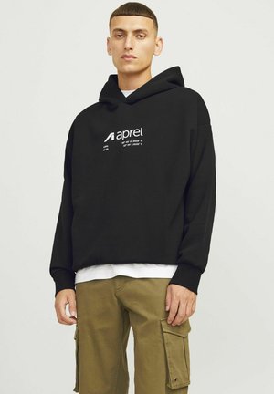 Black hoodie with a front kangaroo pocket, featuring white text and logo. Worn over a white shirt, paired with olive cargo pants.