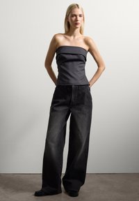 Top gris sin tirantes con un frente plisado, combinado con pantalones vaqueros de pierna ancha en negro. Textura de tela suave con un diseño minimalista.
