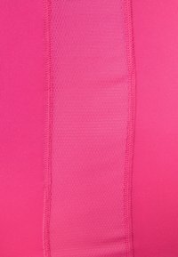 Tela atlética en fucsia, con una textura suave y una sección acanalada en contraste. Un detalle de costura corre verticalmente a lo largo del costado.