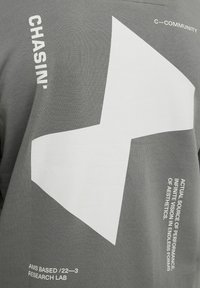 T-shirt grigio con un grande design astratto bianco, con dettagli in bianco sul maniche e sul lato inferiore, realizzato in morbido materiale di cotone.