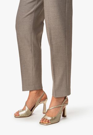 Heeled sandals in metallic gold texture with an open toe and crisscross straps. Paired with light gray tailored trousers.