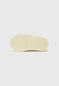Sole in gomma crema con righe orizzontali, con logo centrale. Il design è piatto con punta arrotondata.