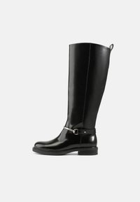 Botas de couro pretas brilhantes até ao joelho com um design simples, apresentando uma corrente e fivela de metal prateado perto do tornozelo. Sola de borracha plana.