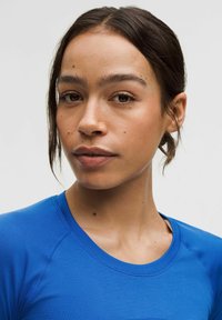 Sinine spordipoolkamage, millel on ümar kaelus ja lühikesed varrukad. Sile tekstuur ja külge liibuv disain, mis toob esile kaeluse ja õmblused õlgadel.