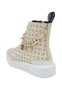 Beige high-top sneaker met een patroonontwerp. Voorzien van gouden kettingaccenten met bedels, een witte zool en een zwarte lus aan de hak.