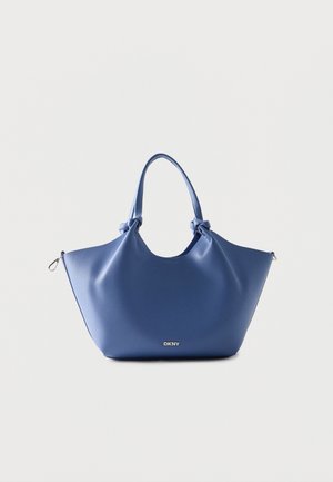 Blå læder tote taske med knuder på håndtagene og sølv DKNY-logo foran, mod en ensartet lys baggrund.