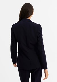 Marinblå Blazer med skräddarsydd passform, enkel slits och långa ärmar. Slät tyg; har en notch-lapel och minimala sömdetaljer.