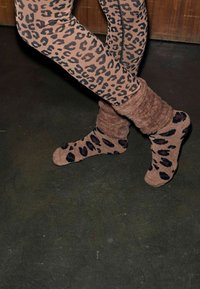 Beige Leggings mit Leopardenmuster und schwarzen Punkten, kombiniert mit braunen, flauschigen Socken mit passenden schwarzen Leopardenpunkten.