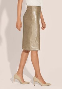 Knie langer Bleistiftrock aus goldenen Pailletten. Glatte Textur, eng anliegende Silhouette, kombiniert mit beigen High Heels.