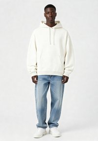 Krema krēkā ar priekšējo kabatu, ar kapuci, kas piestiprināma ar auklām, un ribotiem apkaklītes galiem, saskaņota ar gaiši ziliem džinsiem un baltām sporta apaviem. Vienkāršs dizains.