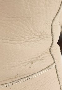 Gros plan sur un cuir beige avec une texture visible, des coutures et une couture avec une légère usure et des traces de saleté.