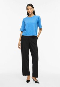 Haut bleu à manches courtes, coupe ample, associé à un pantalon noir taille haute à jambes larges et des escarpins noirs pointus. Couleurs unies, design décontracté.