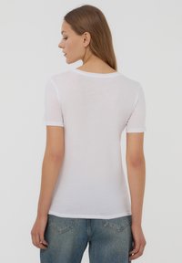 Maglietta bianca a maniche corte realizzata in tessuto leggero e trasparente. Collo arrotondato, design aderente e orlo leggermente curvato sul retro.