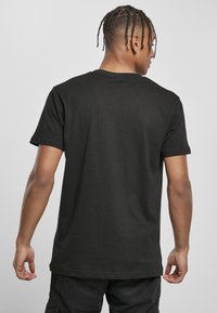 Schwarzes Baumwoll-T-Shirt mit kurzen Ärmeln, klassischem Rundhalsausschnitt und lockerer Passform. Sichtbare Nähte am Saum und an den Ärmeln.