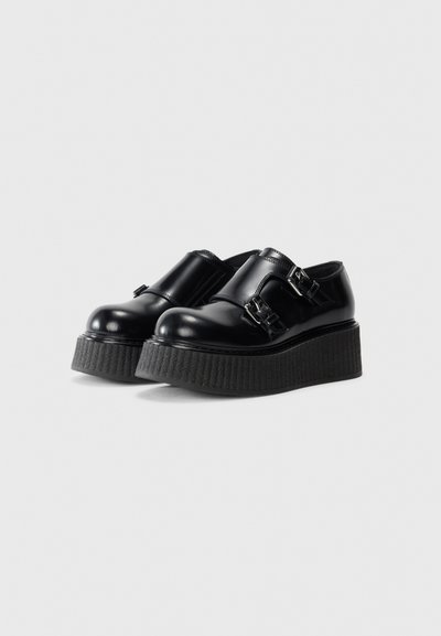 Pair of black leather platform shoes with double silver buckles and thick textured soles on a white background.