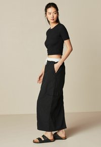 Zwart geribbelde crop top, losse zwarte wijde broek met witte elastische tailleband en zwarte sandalen met kurken zolen.