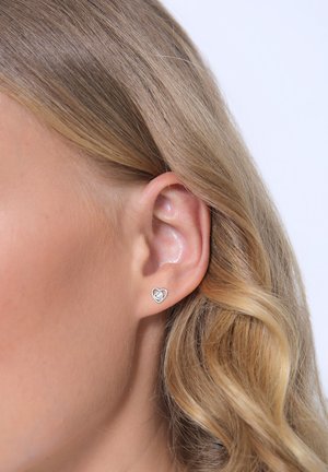 Silberne, herzförmige Steckerohrringe mit einem kleinen inneren Herzdetail. Das Design besticht durch eine glatte metallische Oberfläche und wird am Ohrläppchen befestigt.