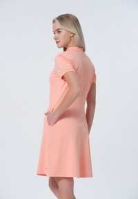 Kraťasové šaty polo stylu z jemného broskvového materiálu s texturou, s bočními kapsami a zakřiveným lemem.