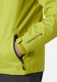 Chaqueta exterior verde brillante en tejido suave, con un bolsillo con cremallera y detalle en el puño de velcro; logo impreso en la manga.