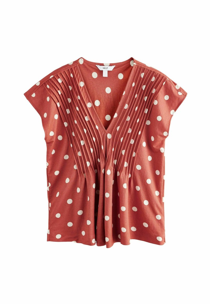 Blouse couleur rouille avec des pois blancs, un décolleté en V, des manches courtes et des plis verticaux à l'avant pour texture et fluidité.