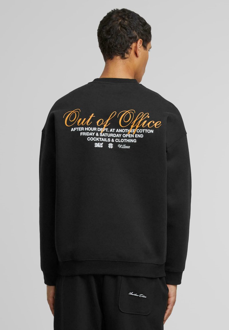 Sudadera de algodón negra con texto gráfico en blanco y naranja en la parte trasera. El diseño incluye un corte casual con puños y dobladillo acanalados.