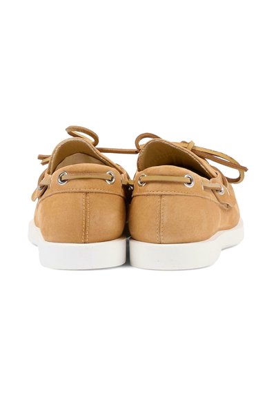 Paire de chaussures bateau en daim beige avec semelles blanches, lacets passés à travers des œillets métalliques, vues de dos sur un fond blanc.