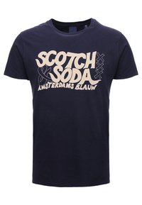 Marineblauwe katoenen t-shirt met een groot cremekleurig grafisch tekstontwerp dat "SCOTCH & SODA AMSTERDAMS BLAUW" zegt, vergezeld van abstracte accenten.