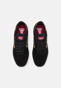 Czarne zamszowe sneakersy z złotymi akcentami, okrągły nosek, czarne sznurówki i czerwone wkładki z napisem "INDEPENDENT" na górze.