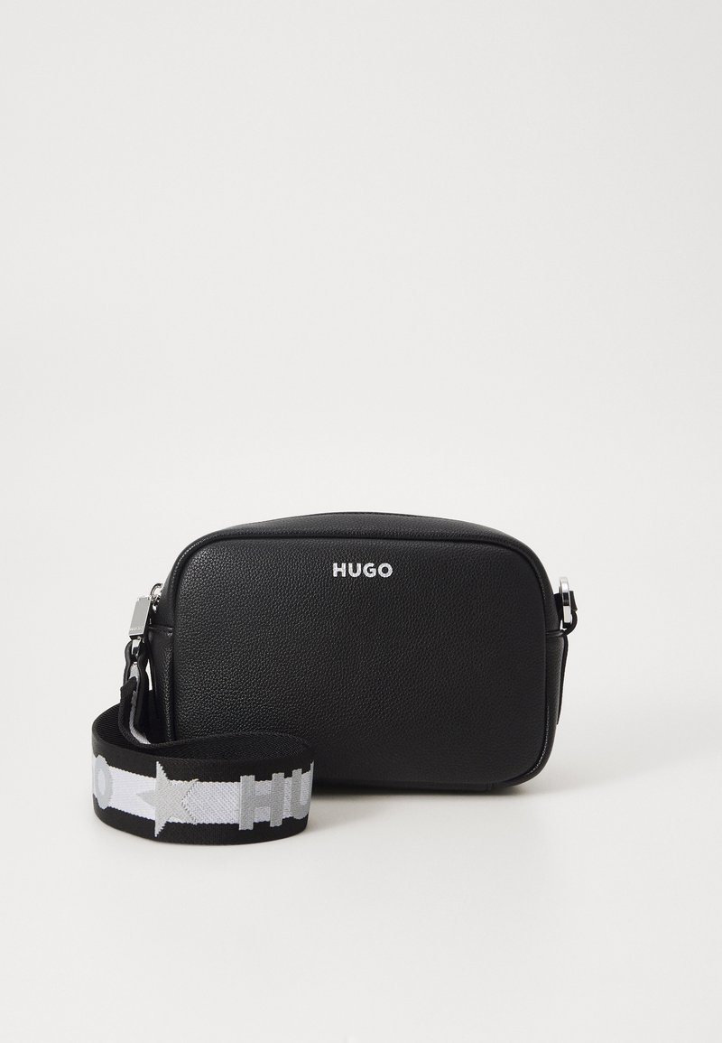 Svart lær crossbody-veske med rektangulær form, utstyrt med et sølvlogo og en kontrastfarget mønstrete stoffreim.