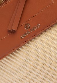 Pruun sünteetiline nahk ja punutud heina käekott kuldse "ANNA FIELD" logo, tekstureeritud pind ja kahekordsed tupsud tõmbluku peal.