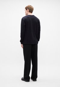 Cămașă neagră cu mânecă lungă și pantaloni negri largi, dintr-un material neted; prezintă un gât rotund și un stil de design minimalist.