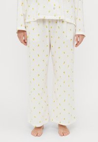 White pajama set with yellow lemon print, featuring a ribbed texture. Loose-fitting trousers with an elastic waistband and buttoned top.