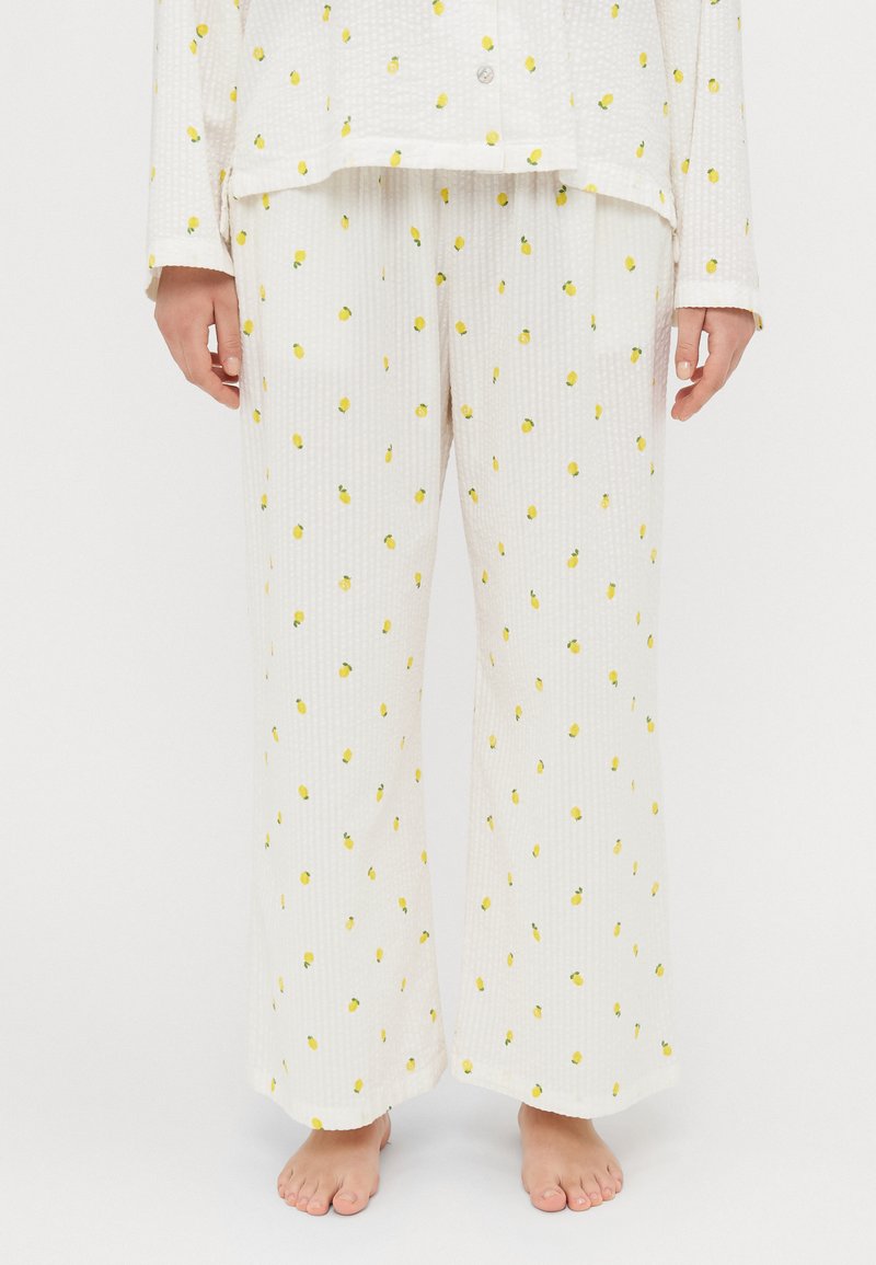 White pajama set with yellow lemon print, featuring a ribbed texture. Loose-fitting trousers with an elastic waistband and buttoned top.
