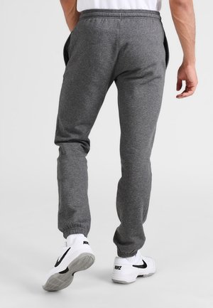 Graue Sweatpants aus weichem Stoff, mit elastischem Bund, seitlichen Taschen und gerippten Bündchen. Kombiniert mit weißen Turnschuhen.