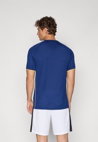 Navy blue athletic shirt with short sleeves and yellow trim, made from breathable fabric, paired with white shorts.