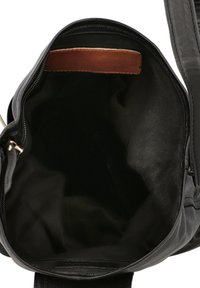 Schwarze Leder-Bucket-Bag, geöffnet, um das geräumige leere Innere mit schwarzer Stofffütterung und einem kleinen rechteckigen braunen Lederpatch innen zu zeigen.