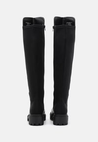 Botas negras hasta la rodilla con un upper sintético liso, cremalleras traseras, suelas de goma texturizadas y detalles de costura decorativa.