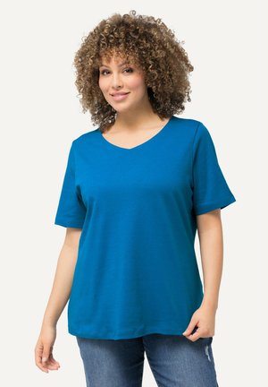 Camiseta de algodón de manga corta y escote en V color verde azulado, fabricada con un tejido suave; corte relajado y textura suave; combinada con jeans azules que muestran un ligero desgaste.
