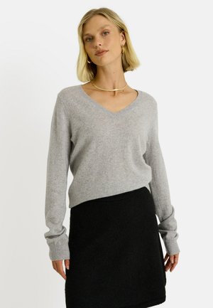 Suéter gris claro con cuello en forma de V, hecho de un material de punto suave y de manga larga, combinado con una minifalda negra con textura. Diseño simple, sin patrones.