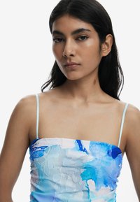 Haut sans manches à motifs floraux bleus avec des bretelles fines, présentant une texture lisse et un design froncé, principalement dans des nuances de bleu et de blanc.