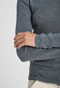 Top gri cu dungi, cu mâneci lungi, din tricot, cu manșete ajustate și textură moale, cu o croială lejera la tiv și detalii subtile.