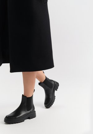 Czarne botki Chelsea wykonane z teksturowanej skóry, z elastycznymi panelami po bokach i chunky, ryflowaną podeszwą. Projekt jest elegancki i nowoczesny.