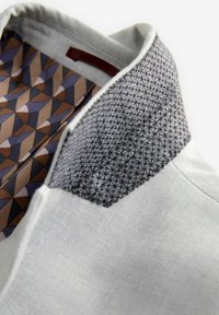Camisa de cuello con tejido gris y un collar negro texturizado. En el interior presenta un patrón geométrico en tonos marrones, beige y morados.
