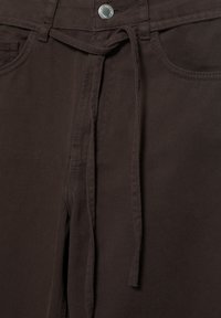 Dunkelbraune Hose mit vorderem Knopf, sichtbaren Gürtelschlaufen, Seitentaschen und einem gebundenen Stoffgürtel an der Taille.