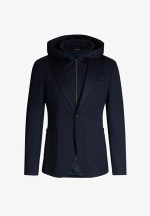 Blazer bleu marine avec capuche détachable, deux poches avant, fermeture à un bouton et texture subtile. Intérieur doublé en tissu coordonné.